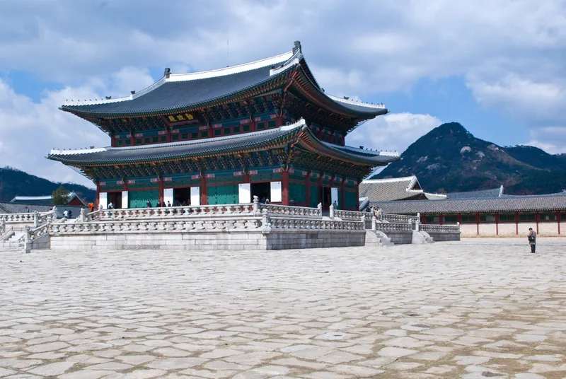 Điện Geunjeongjeon uy nghi trên nền đá trong Cung điện Gyeongbokgung ở Seoul, phía sau là núi non.