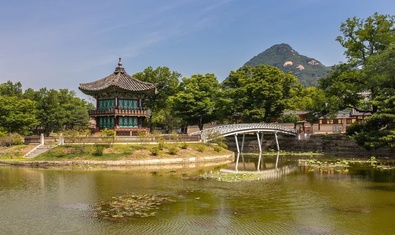 Đình Hyangwonjeong và cây cầu cong bắc qua hồ sen, phía sau là núi non ở Seoul.