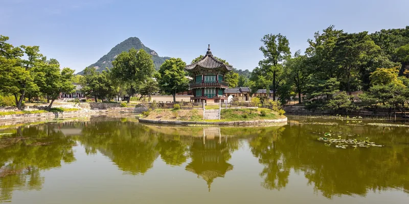Một đình cổ nằm trên hòn đảo nhỏ giữa hồ nước, phản chiếu rõ nét, với đỉnh núi phía sau tại Seoul.