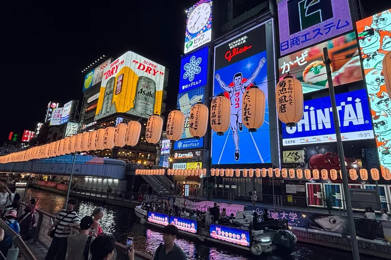 Biển hiệu neon và đèn lồng thắp sáng kênh Dotonbori ở Osaka vào ban đêm khi thuyền đi qua.