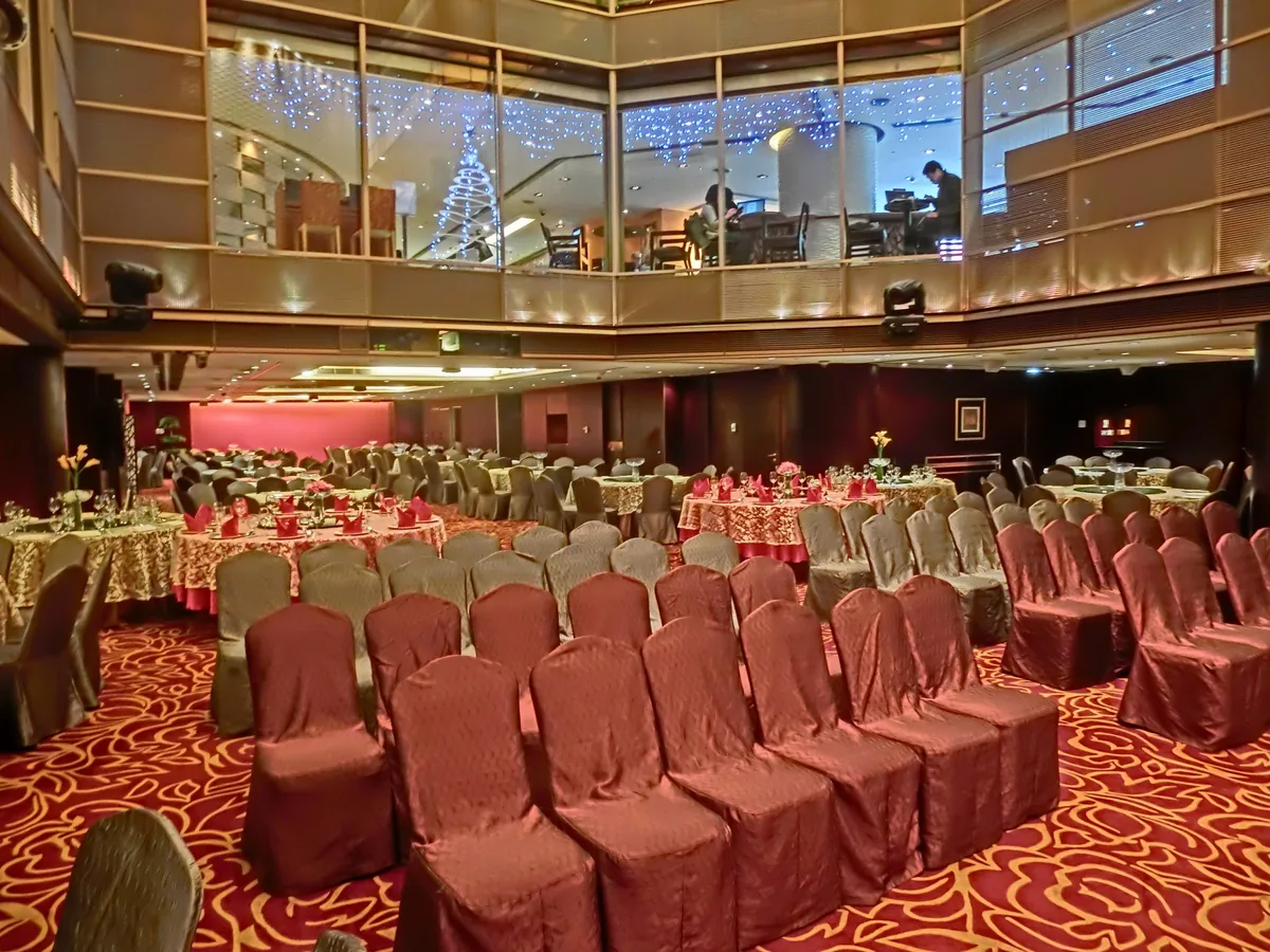 Một phòng tiệc khách sạn ở Hồng Kông được bày hàng ghế bọc vải và các bàn tròn dưới giếng trời kính.