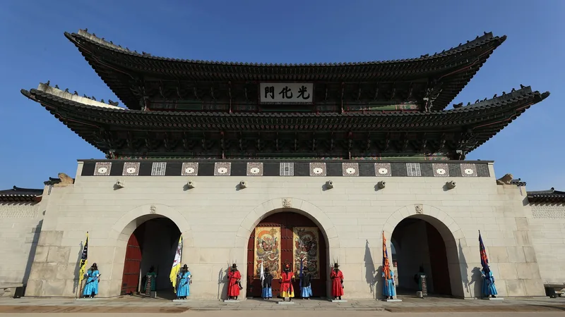 Lính gác trong trang phục truyền thống đứng trước các cổng mái vòm của Gwanghwamun ở Seoul dưới bầu trời xanh.