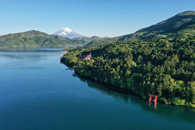 Cổng torii đỏ nổi trên hồ Ashi với núi Phú Sĩ phía xa giữa những ngọn đồi xanh ở Hakone.