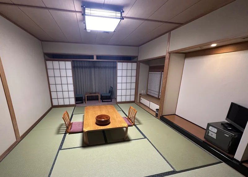 Phòng kiểu ryokan truyền thống Nhật Bản với sàn tatami, cửa trượt shoji và bàn gỗ thấp có ghế.