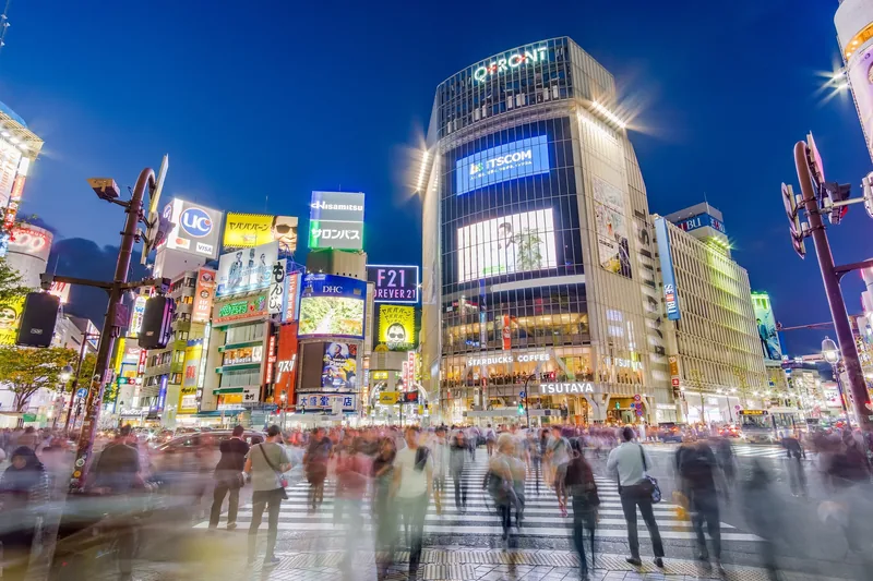 Biển hiệu neon rực rỡ trên các tòa nhà khi người đi bộ băng qua giao lộ Shibuya về đêm ở Tokyo