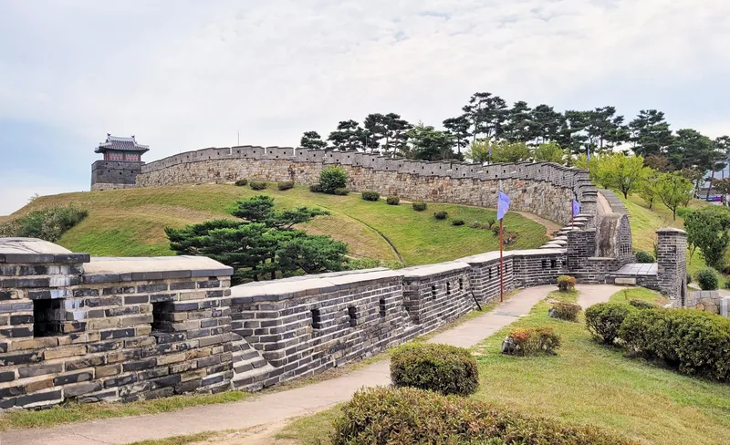 Tường thành đá của pháo đài Hwaseong uốn lượn trên đồi cỏ ở Suwon, với vọng gác phía xa.