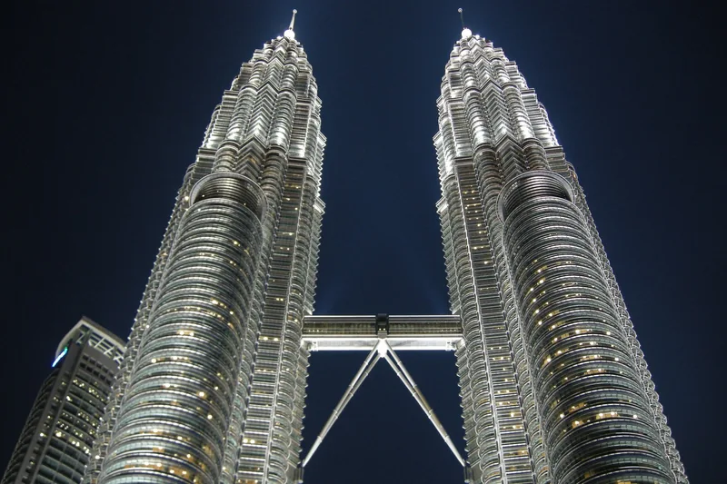 Góc nhìn từ dưới lên tháp đôi Petronas sáng đèn cùng cầu nối trên nền trời đêm ở Kuala Lumpur.