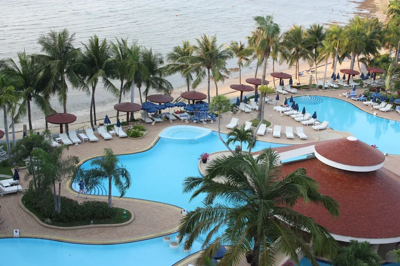 Toàn cảnh hồ bơi khu nghỉ dưỡng ven biển với hàng cọ và ghế tắm nắng tại Pattaya, Thái Lan.